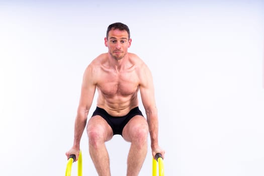 Front and side view photo of strong young man exercising on parallel bars in studio.