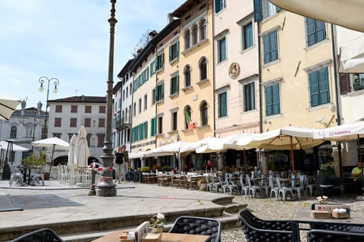 Colonnade and path, square of the freedom in Italian city Udine. People strolling the cobblestone alley on a beautiful sunny summer day. Italy. People. Lifestyle. Tourism. August 2023