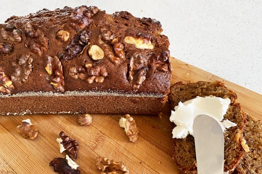Banana sweet bread sliced on a wooden cutting board with walnuts. Slice of banana bread with cream cheese.