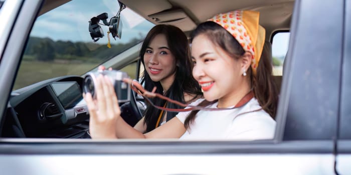 Cheerful female start smiling friends going on a trip while woman friends sticking head out of car in motion to see the view traveling.