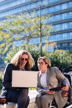vertical photo of a business man and woman using wheelchair smiling happy while working outdoors with laptop and tablet, concept of diversity and urban lifestyle, copy space for text