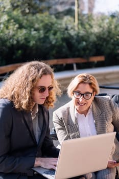 business man and smiling woman using wheelchair working outdoors with laptop and tablet, concept of diversity and urban lifestyle