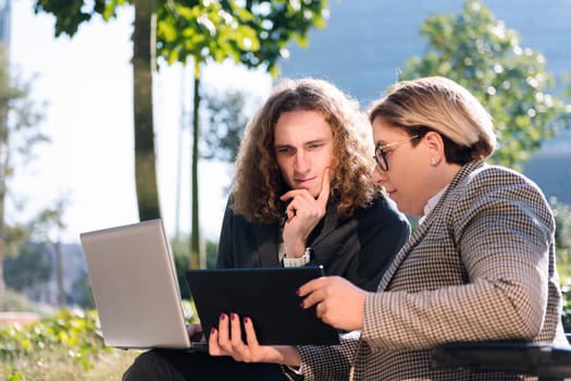 young businessman and businesswoman using wheelchair working outdoors with laptop and tablet, concept of diversity and urban lifestyle