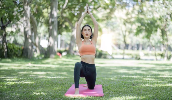 Attractive and charming Asian woman in her 30s in sportswear doing yoga poses, relaxing muscles. Asian woman practicing yoga in a beautiful green park.