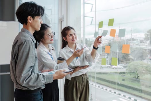 team employees busy brainstorming develop business ideas write on colorful sticky notes, concentrated colleagues share thoughts on pads on glass window.