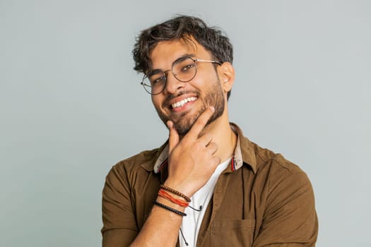 Cheerful lovely happy young Indian man smiling friendly glad expression looking at camera dreaming resting relaxation feel satisfied good news. Arabian bearded guy isolated on gray studio background