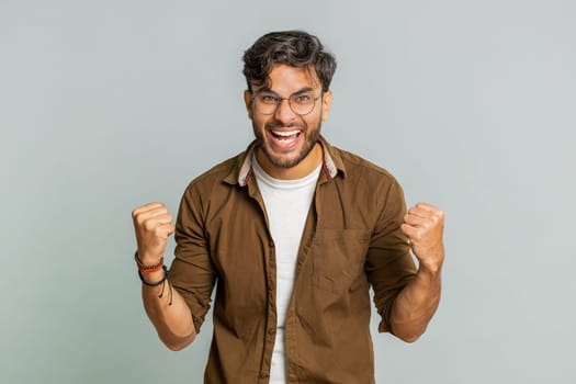 Happy joyful Indian man celebrating success victory, winning birthday, lottery jackpot goal achievement play game good positive news, triumph. Young Arabian guy isolated on gray studio background