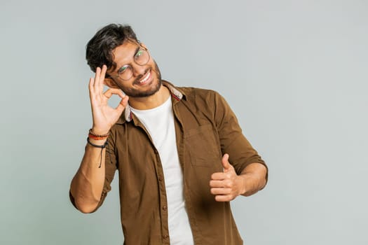 Okay. Happy Indian man looking approvingly at camera showing ok gesture, like sign positive feedback, approve something good, celebrate victory, wink blink eye flirting. Arabian guy on gray background