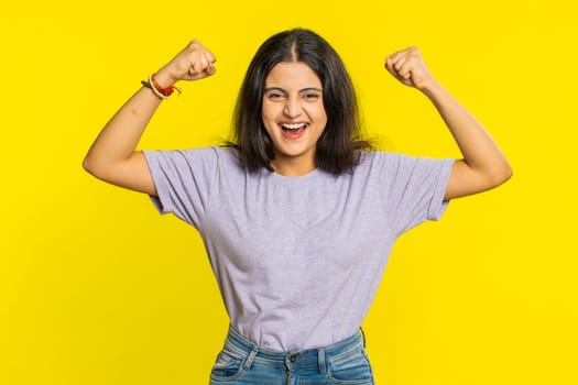 I am strong and independent. Young Indian woman showing biceps and looking confident, feeling power strength to fight for rights, energy to gain success win. Girl isolated on yellow studio background