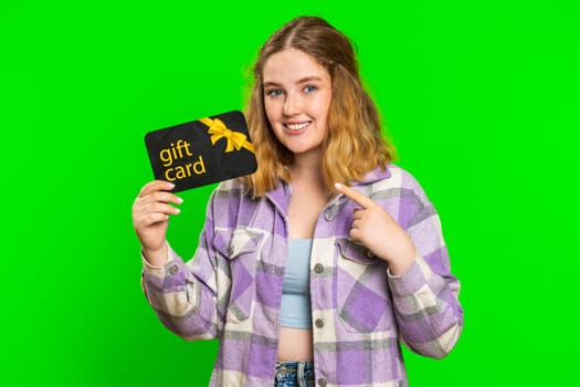 Happy caucasian woman showing pointing on gift discount certificate voucher coupon for store holidays sale. Redhead girl with shopping christmas surprise card isolated on green chroma key background