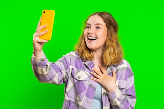 Happy young caucasian woman blogger taking portrait selfie on smartphone, communicating record video call online with social media subscribers. Redhead girl isolated on green chroma key background