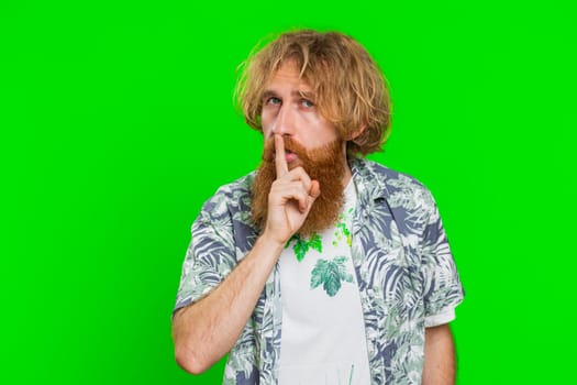 Shh be quiet please. Young man presses index finger to lips makes silence gesture sign do not tells secret, stop talk gossip confidential privacy. Redhead bearded guy isolated on chroma key background