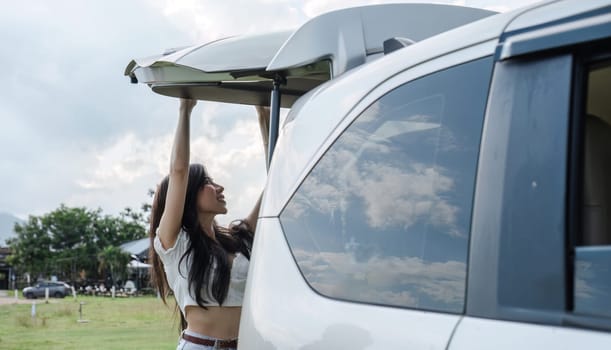 A beautiful young woman, sightseeing in nature, traveling by car on vacation, is closing the back door of the car to store things used in the travel trip. Traveling by private car.