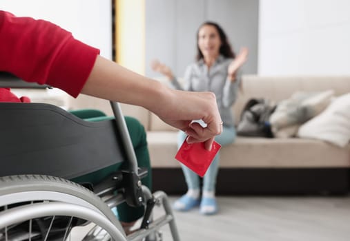 Person sitting in wheelchair holds red condom in his hand in front of woman sitting. Safe and Responsible Sexual Behavior