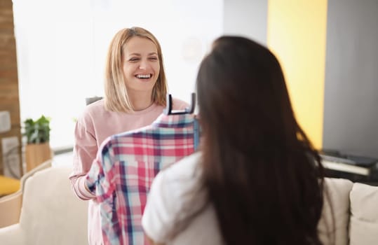 Smiling woman demonstrates clothes on hanger to client. Atelier for tailoring and repairing clothes concept