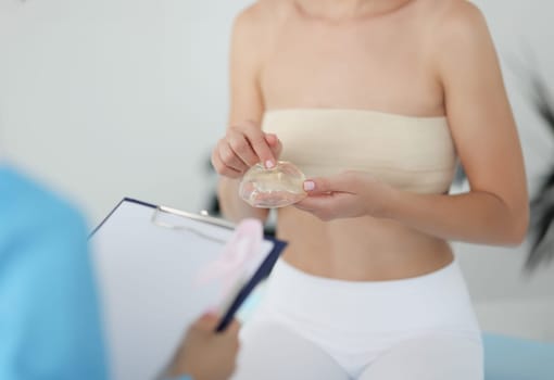 Woman at doctor's appointment is holding breast silicone implant. Breast enlargement surgery concept