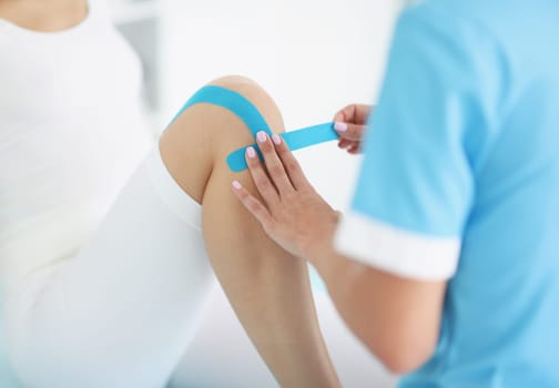 Doctor glues kinesio tape to patient's knee. Injuries and sprains of joints and muscles concept