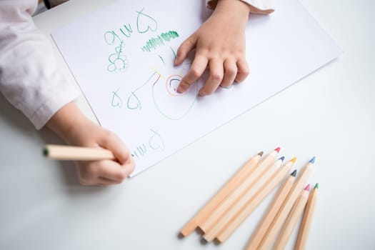 Child drawing with colored pencils on white paper.
