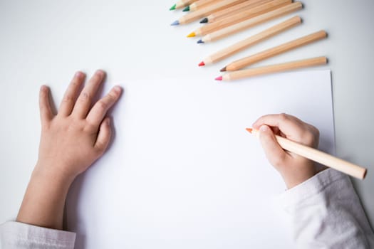 Childs hands drawing with colored pencils on white paper.