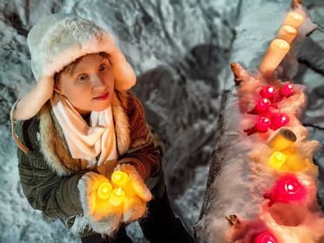 A middle-aged woman strolls through a snowy forest at night, warmly dressed with candles, bringing a playful and lighthearted mood.