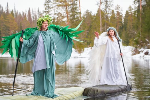 Two girls in white and green dresses embody the magical transition from winter to spring while standing on a serene lake.