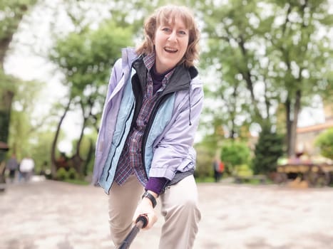 Middle-aged woman captures joyful selfies in a lush park while on a journey to explore nature and enjoy the outdoors.
