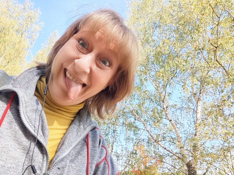 Blonde woman enjoys a joyful moment outdoors during her autumn nature trip, surrounded by colorful foliage and clear skies.