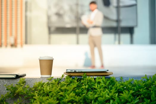 A takeaway coffee cup, a laptop and documents on a bench in front of a building.