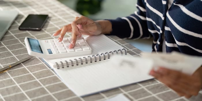 A focused young woman uses a calculator to manage her finances and bills, highlighting the importance of budgeting and financial literacy.