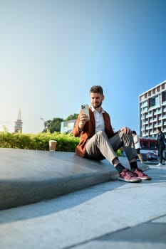 Smiling caucasian male investor using smartphone in an outdoor city space.