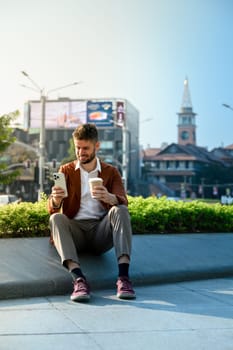 Smiling caucasian male investor using smartphone in an outdoor city space.