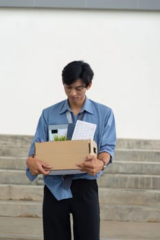 A young professional reflects on his career change as he carries a box of personal items out of the office.