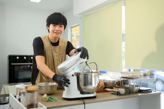Smiling young baker preparing cookie dough and using a stand mixer in a kitchen.