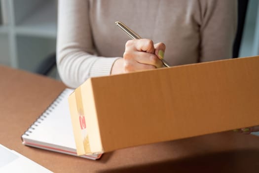 A joyful Muslim woman in a hijab manages her online sales, speaking on the phone and surrounded by packages in her home office.