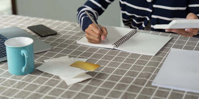 A person reviews bills and calculates income at home, using a notebook and calculator for financial planning.