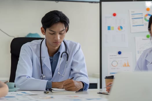 A doctor actively participates in a meeting, taking notes while discussing healthcare strategies and data analysis with the team.