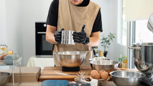 Male baker sifting flour for chocolate chip cookies dough over kitchen counter.