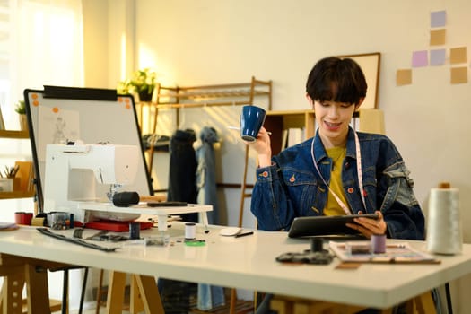 Designer holding a cup of coffee and using digital tablet in a creative studio.