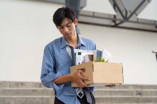 A professional man holds a box of personal items, signifying a major career shift as he exits the workplace.
