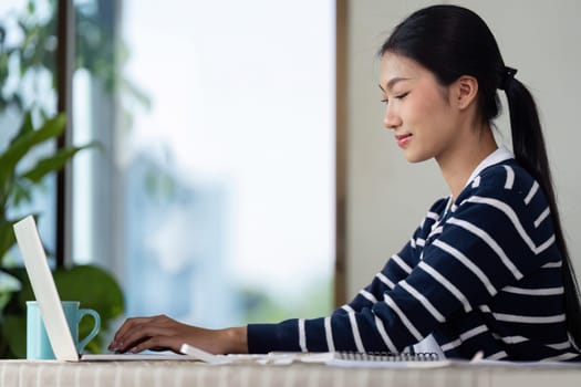 A young woman works on her laptop while managing her finances and bills at home, illustrating modern financial management.