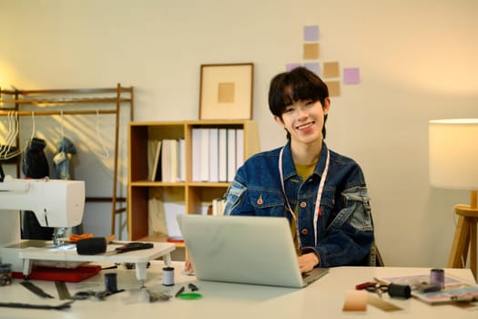 Smiling fashion designer working on a laptop in a studio.