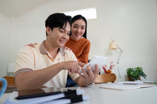 A couple smiles while reviewing financial information on a tablet, showcasing teamwork in managing their finances.