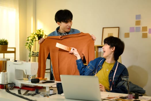 Two young fashion designers comparing fabric colors in a creative studio.