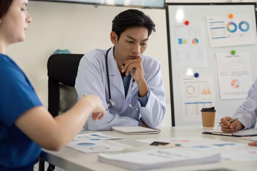 A diverse group of healthcare professionals, including a physician and nurse, analyze charts and discuss strategies during a meeting.