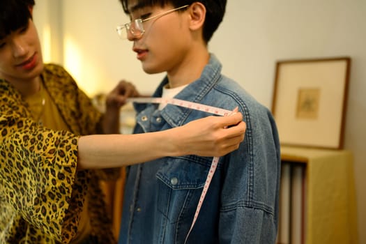 Tailor measuring a client shoulder with measuring tape for custom clothing.