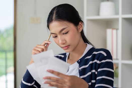 A young woman thoughtfully reviews her financial documents and bills at home, focusing on budgeting and financial literacy.