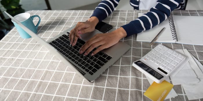 A young woman reviews financial documents while using a calculator and laptop, illustrating the importance of budgeting and financial planning.