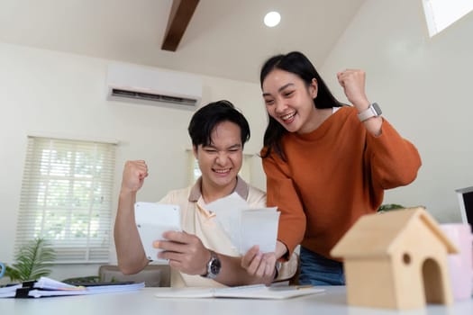 A happy couple enthusiastically reviews their finances, celebrating their income calculations and budgeting achievements.