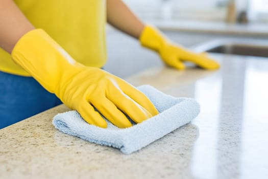 Woman in protective yellow gloves washing kitchen table with cloth. Housework concept.