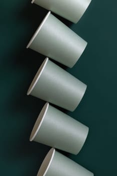 Disposable light green paper cups on a dark green background top view, mockup with advertising copy space. Empty cardboard coffee cups flat lay. No plastic and sustainable lifestyle concept
